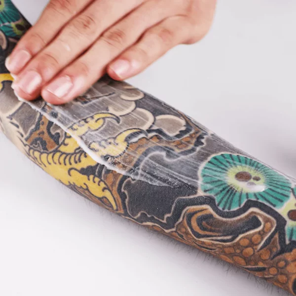 Hand applying lotion on a tattooed arm.