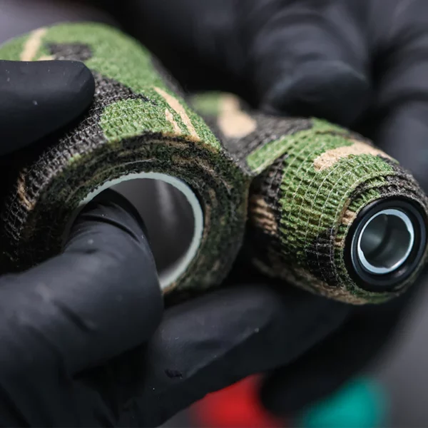 Gloved hands holding camouflage-patterned tape rolls.