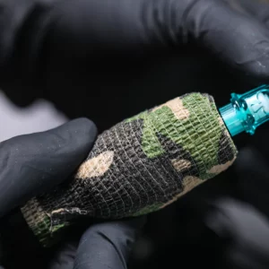 Gloved hands holding a camo-patterned tattoo machine.