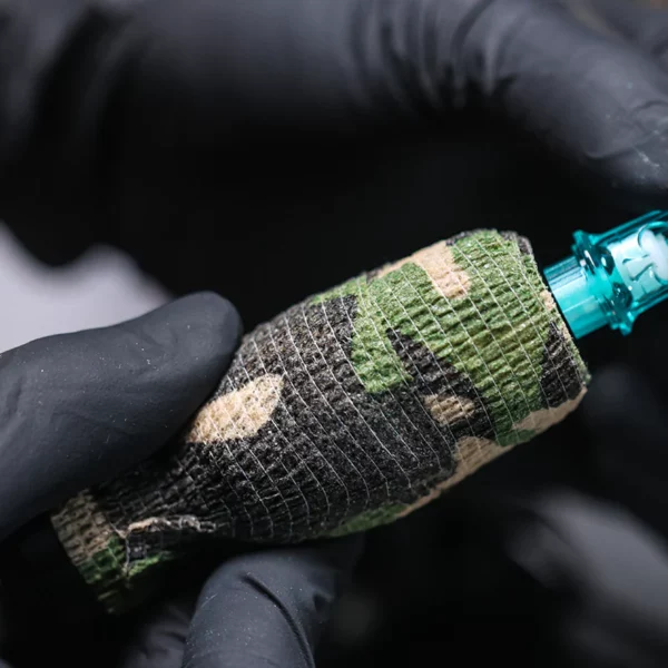 Gloved hands holding a camo-patterned tattoo machine.
